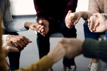 Close-up of group of people holding hands during psychotherapy session.