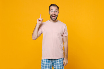 Excited young bearded man in pajamas home wear hold index finger up with great new idea resting at home isolated on bright yellow colour background studio portrait. Relax good mood lifestyle concept.