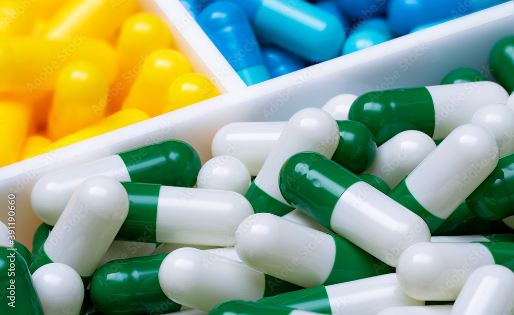 Poster selective focus on green-white capsule pills in plastic box on blurred blue and yellow capsule pills