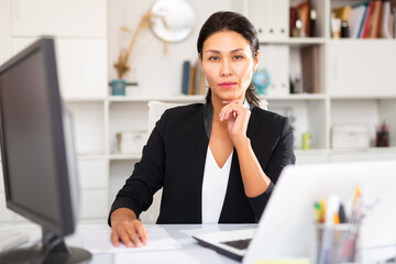 Woman manager working with laptop and documents at table in office interior..