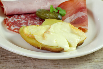 fromage à raclette fondu sur une pomme de terre et charcuterie dans une assiette