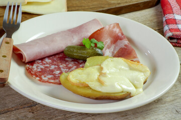fromage à raclette fondu sur une pomme de terre et charcuterie dans une assiette