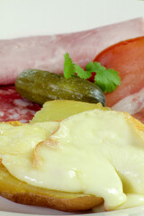 fromage à raclette fondu sur une pomme de terre et charcuterie dans une assiette