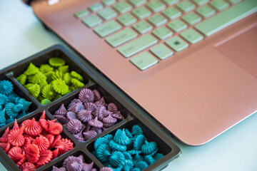 Close up Allure Thai handmade candy in a brown plastic box next to a pink laptop on a white table next to the window.