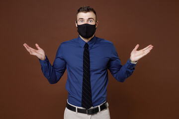 Shocked young business man in blue shirt tie face mask to safe from coronavirus virus covid-19 spreading hands isolated on brown background studio portrait. Achievement career wealth business concept.