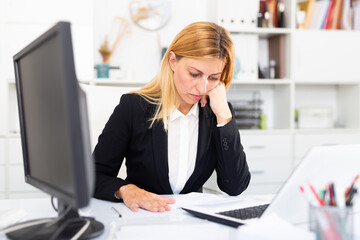 Focused young woman working with laptop and documents in modern office