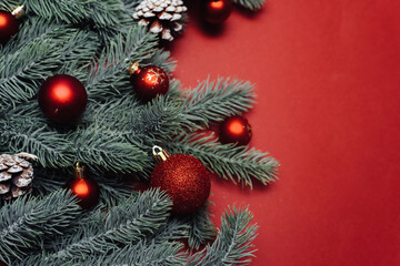 Fototapeta na wymiar Space for text between Christmas tree branches with Christmas decorations and balls on a red background. Christmas composition. Happy New Year. Space for text