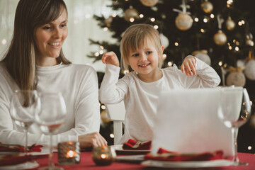 A happy family with a child is celebrating Christmas with their friends on video call using webcam. Family greeting their relatives on Christmas eve online. New normal
 virtual event