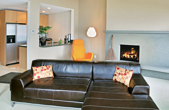 Open plan living room and kitchen in a modern home, a lit fire and sectional sofa. 

