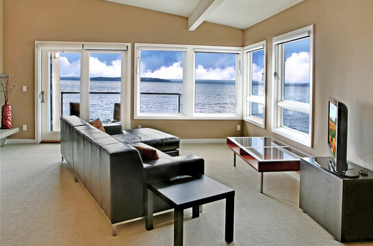 A living room in a waterfront house, with a large window and an ocean view. 
