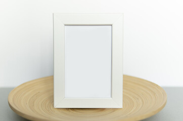 Mockup of a portrait white frame on a bamboo plate on a beige and gray paper background. Scandinavian style.