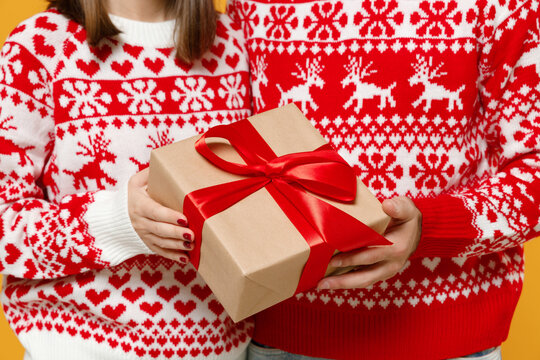 Cropped image of young Santa couple friends man woman in Christmas red sweater hold present box with gift ribbon bow isolated on yellow background studio. Happy New Year celebration merry concept.