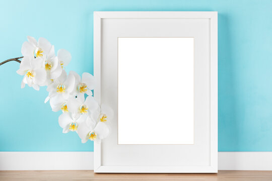 Elegant poster artwork mockup template for online shop with white vertical picture frame with matte and orchid branch in front of pastel green wall. Blank image area isolated with clipping path.