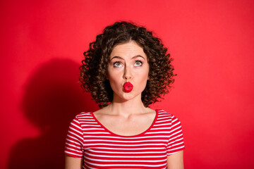 Photo of funny flirty young woman dressed striped outfit looking up empty space lips pouted isolated red color background