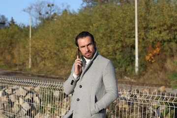 Fototapeta Stylowo ubrany przystojny, dojrzały  mężczyzna z telefonem na peronie. obraz