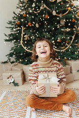 5 years girl sitting under christmas tree and holding christmas gift.