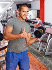 Positive sporty guy doing exercises with dumbbells at sports club