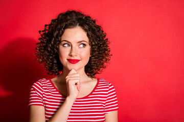 Photo of pretty dreamy curly young lady wear casual striped outfit arm chin looking empty space isolated red color background