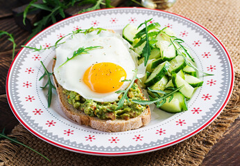 Healthy breakfast. Christmas brunch. Avocado sandwich with fried egg and cucumber with arugula on wooden table.