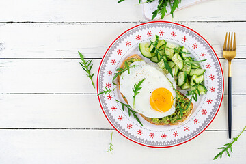 Healthy breakfast. Christmas brunch. Avocado sandwich with fried egg and fresh salad cucumber with arugula for healthy breakfast or snack. Top view, copy space