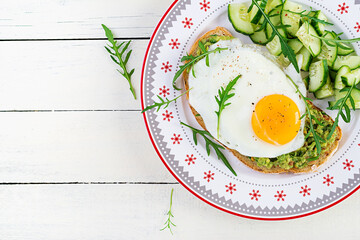 Healthy breakfast. Christmas brunch. Avocado sandwich with fried egg and fresh salad cucumber with arugula for healthy breakfast or snack. Top view, copy space