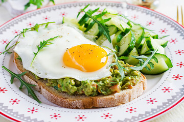 Healthy breakfast. Christmas brunch. Avocado sandwich with fried egg and fresh salad cucumber with arugula for healthy breakfast or snack.