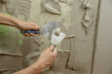 A worker plasters the wall with a spatula and applies a cement mix solution. The repairman lays the...