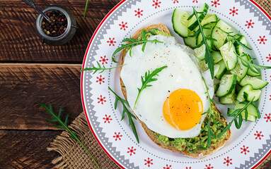 Healthy breakfast. Christmas brunch. Avocado sandwich with fried egg and cucumber with arugula on wooden table. Top view, copy space