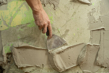 A worker plasters the wall with a spatula and applies a cement mix solution. The repairman lays the...