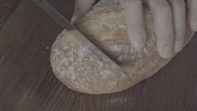 S-Log3. Cutting a loaf of bread on a dark wooden board. Close-up. View from above.