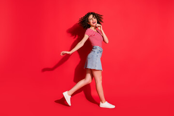 Full body photo of attractive young woman hand touch chin crazy happy enjoy go walk isolated over red color background