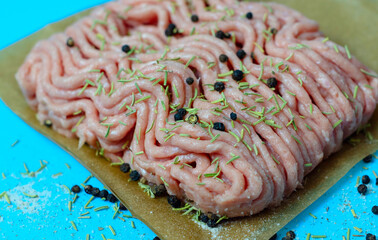 fresh ground turkey meat close up with pepper and rosemary on blue background