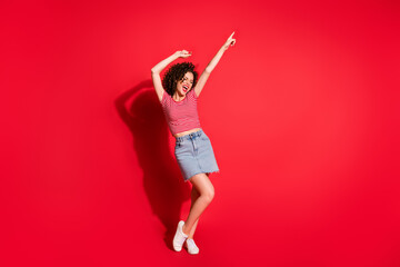Full body photo of young positive girl enjoy point finger empty space yell shout wear mini skirt isolated over red color background