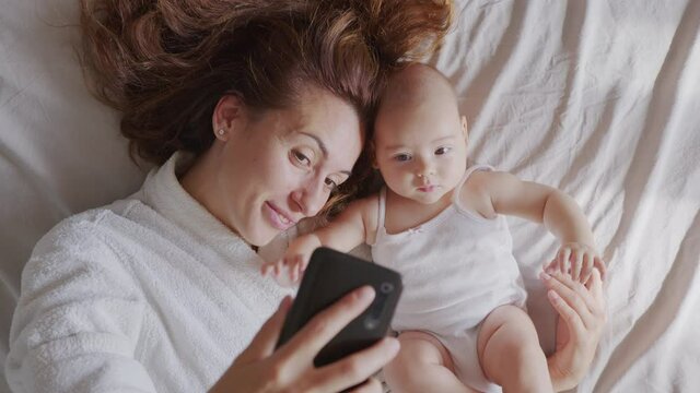 Close up of mother and her newborn baby making a selfie or video call to father or relatives in a bed. Concept of technology, new generation, family, connection, parenthood.
