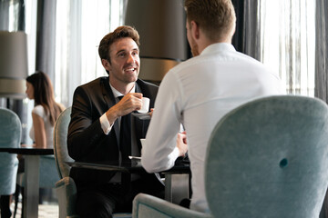 Colleagues and friends. Two cheerful businessmen drinking coffee and talking to each other