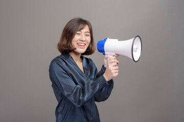 Portrait of young beautiful asian woman holding megaphone over studio background.