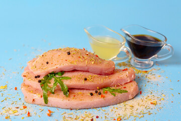 fresh turkey steaks with pepper and arugula on blue background, soy sauce and lemon juice for marinade
