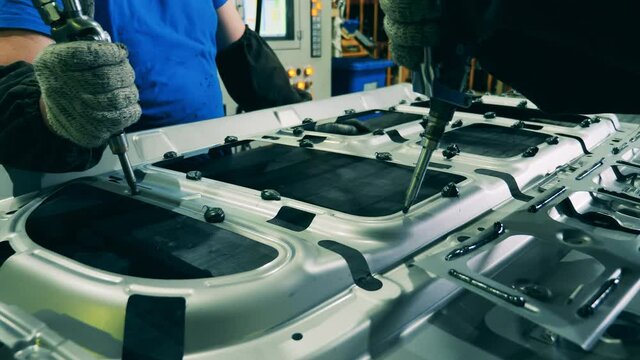 Plant workers are putting glue onto the carcass of a car door
