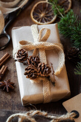 Christmas gift box decorated with burlap ribbon and pine coneswith vintage scissors and festive ornaments at the background. Recycled eco friendly wrapping material or zero waste concept