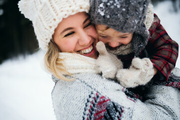 Cheerful mother with small daughter standing in winter nature, laughing.