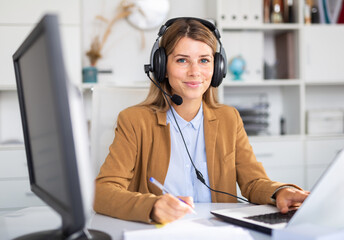 Smiling female operator talking with customer using headset at company office