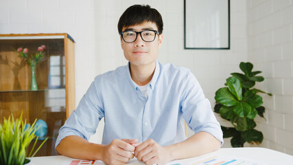 Young Asia businessman using computer laptop talk to colleagues about plan in video call meeting while working from home at living room. Self-isolation, social distancing, quarantine for corona virus.