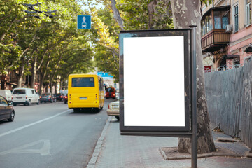 Blank mock up vertical street billboard in busy city street. Yellow bus travels on a dedicated line...