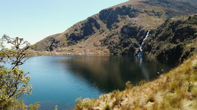 4k daytime video looking over a beautiful deep blue lake and a high waterfall at the 5 Lakes of Pichgacocha, Ambo, Huanuco, Peruvian Andes. Above 4000 meters.  Pan right to left. Wide angle shot.
