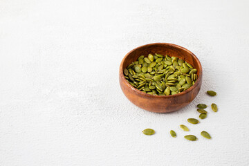 Side view of roasted pumpkin seeds in wooden bowl. Dry Pepita after shelling on white background. Copy space