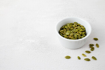 Side view of roasted pumpkin seeds in white bowl. Dry Pepita after shelling on white background. Copy space