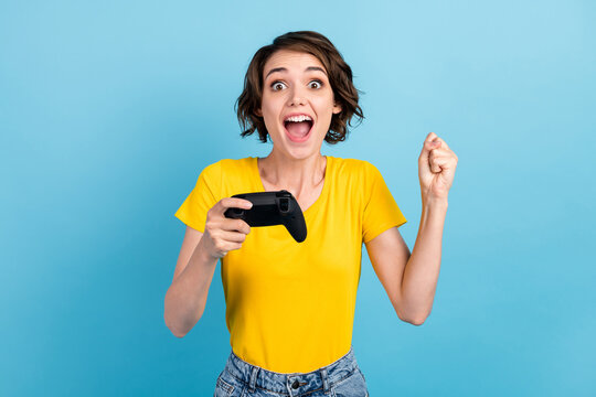 Photo of excited girl hold controller open mouth raise fist wear yellow t-shirt isolated blue color background
