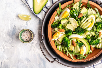 Avocado salad with boiled eggs, broccoli, cucumber, arugula and almond nuts. Vegan, detox Buddha bowl, Delicious breakfast or snack on a light background, top view