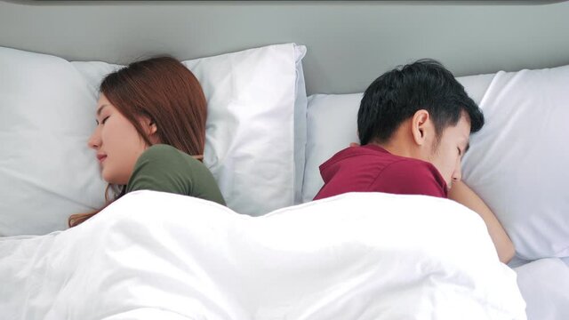 Unhappy Asian couple Lying In Bed having unsolved relationship problems. hotel, travel, relationships, and sexual problems concept. Young Couple worried in problems in the relationship.