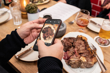 tranchiertes T-Bone Steak fotografiert mit Smartphone am Tisch